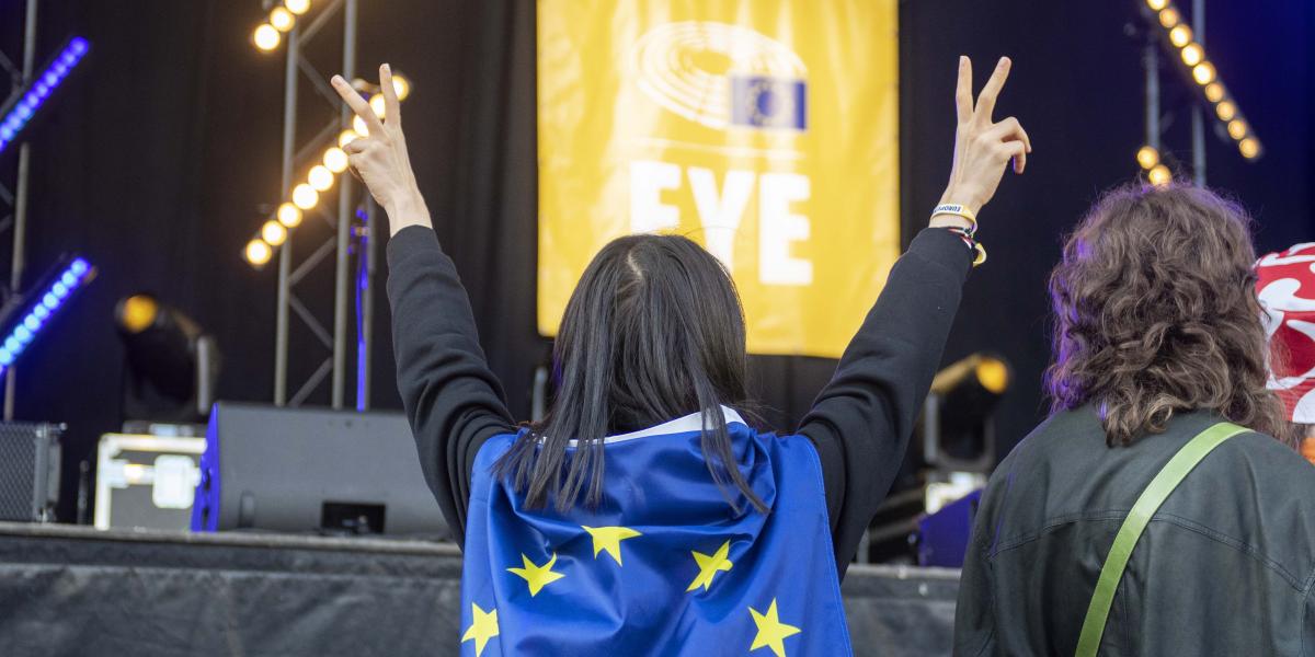 Young women with an EU flag on her back in front of a stage