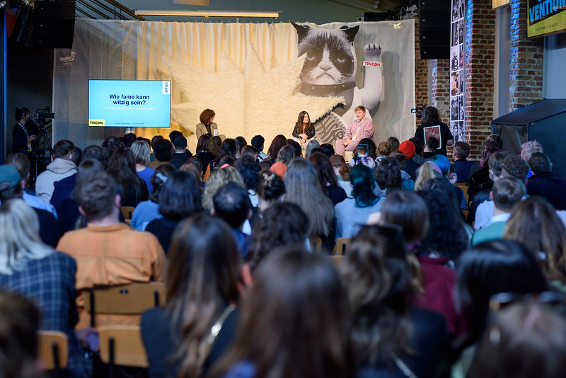 Das Publikum schaut auf die Bühne der TINCON, wo 3 junge Menschen sitzen und sich unterhalten. 