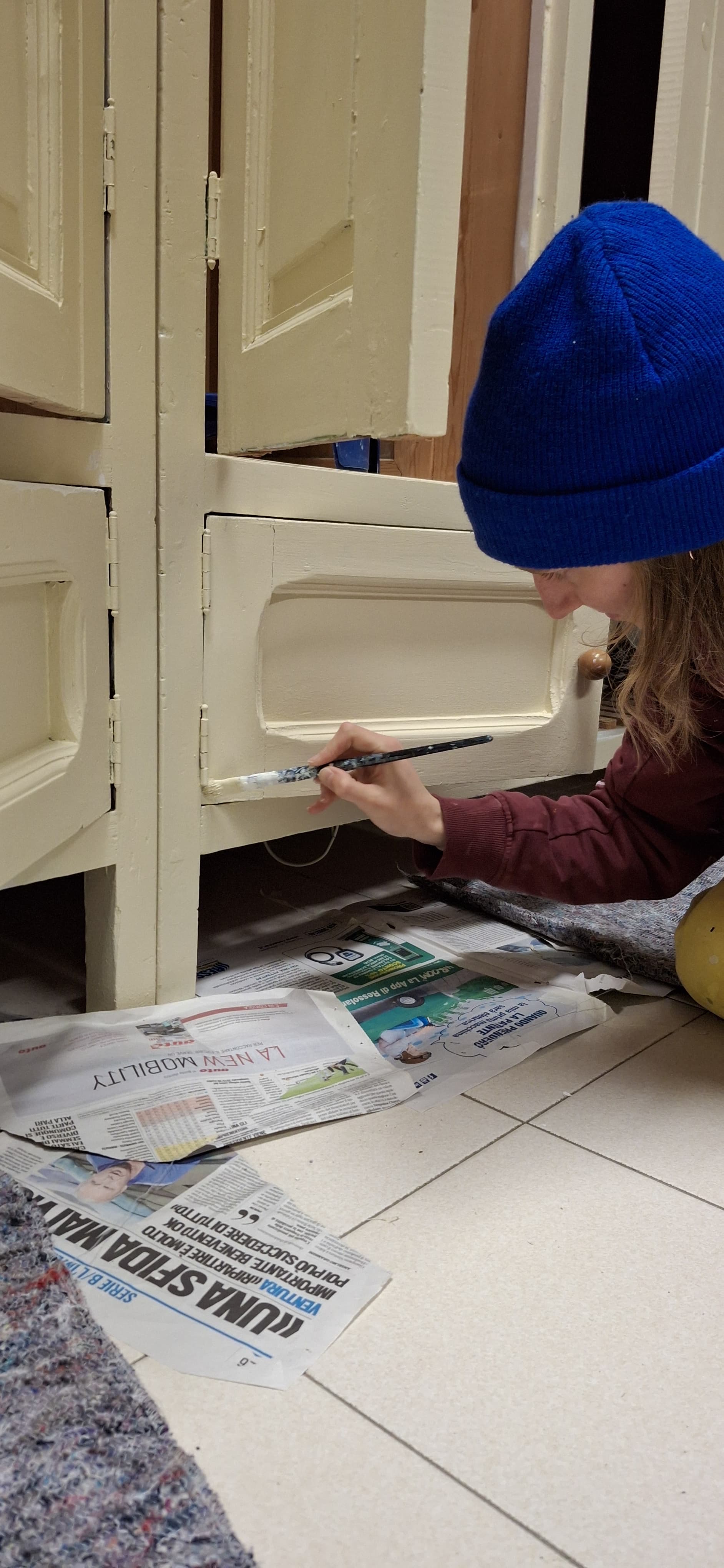 Julie - schilderen van meubels - er ligt krantenpapier op de grond - wit geverfde kast