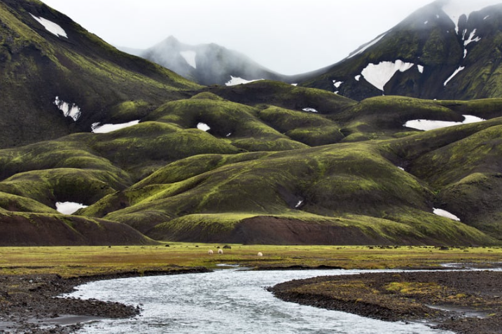 The rugged landscape of Landmannalaugar is surrounded by lush green and snow-dappled hills.   