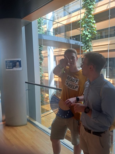 Two men in a bright atrium, one in a yellow shirt pointing, the other listening.