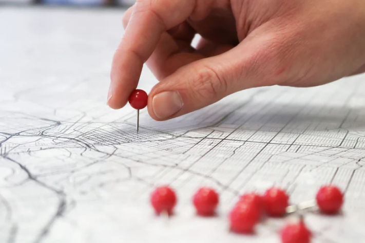 Close-up of a hand pushing a pin into a map.