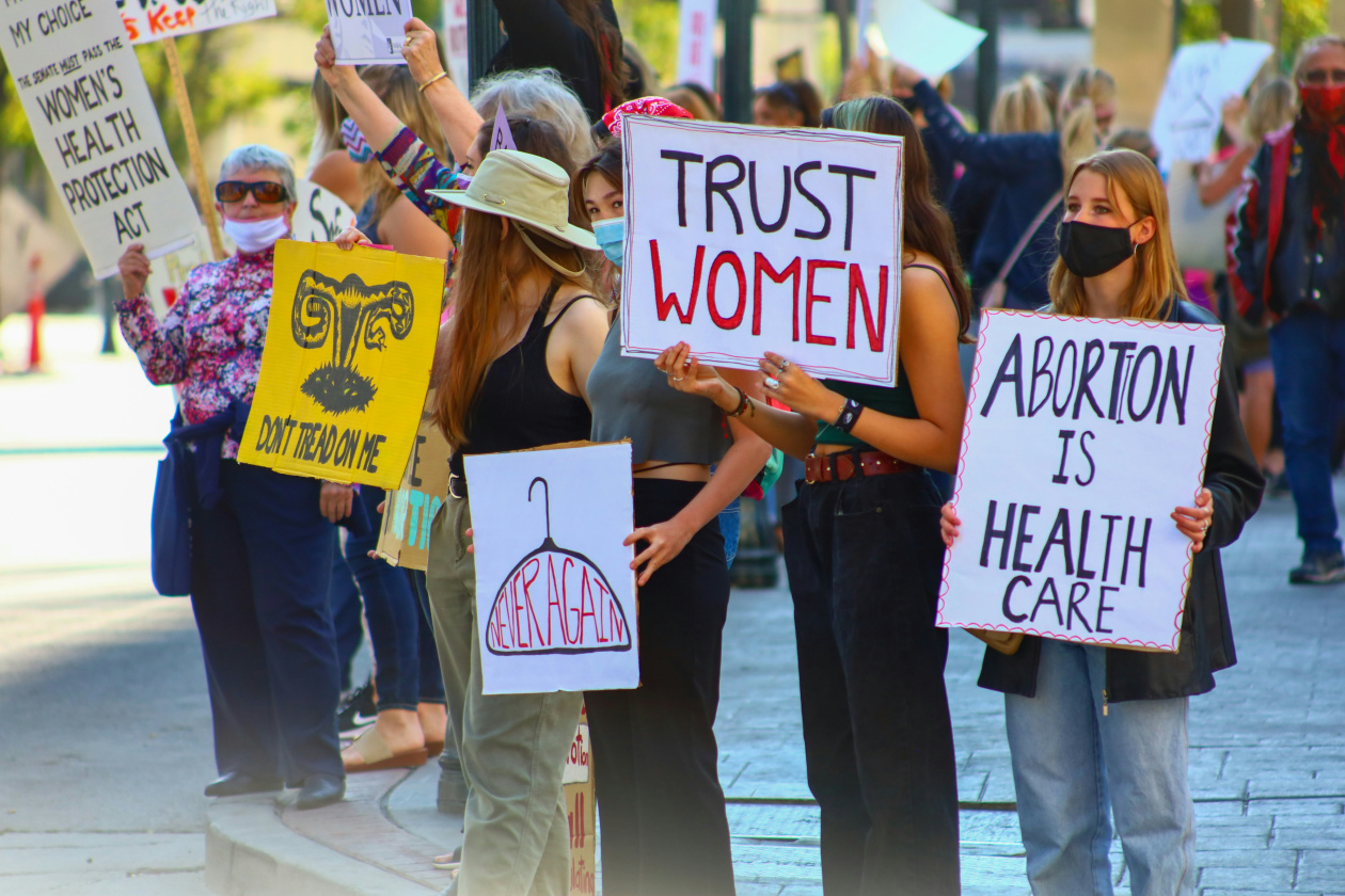 Woman with posters in the street: Trust women / Abortion is health care