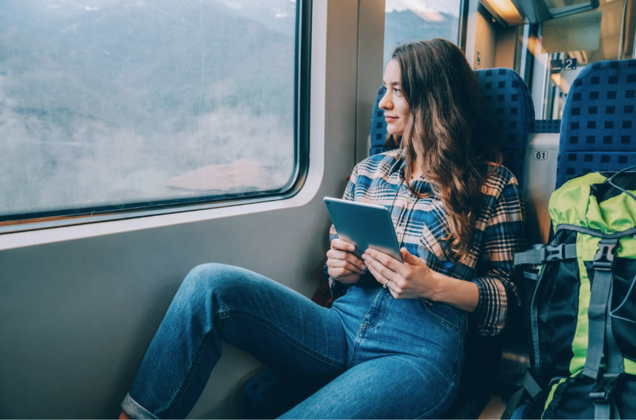A young person holding a tablet, looking at the window, travelling on a train.