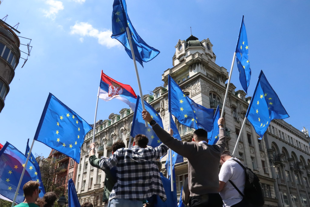 Young people demonstrating, while holding EU and Serbian flags.