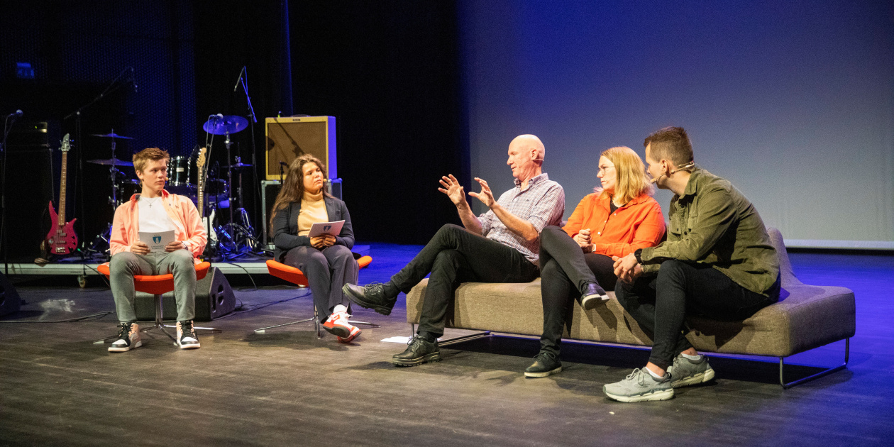 Young and older people on a stage exchanging ideias