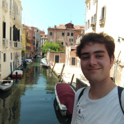 This picture is a selfie of me and  you can see one of the canals of Venice with a few boats