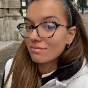 Person with glasses in a white jacket in front of a historic building with arched windows.