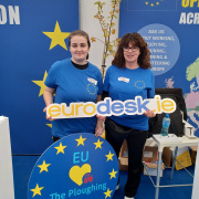 Regan and colleague holding a sign 'eurodesk.ie' with European signage behind them