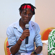 Barasa Daniel holding a microphone speaking during an open debate with politicians and law makers on a campaign against sexual violence