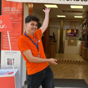 A person wearing an orange shirt stands outside an Alhambra Tickets & Tours office, gesturing towards the entrance.