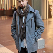 En profilbild på Mohamed som står med en grå jacka och kollar in i kameran med händerna i fickorna.