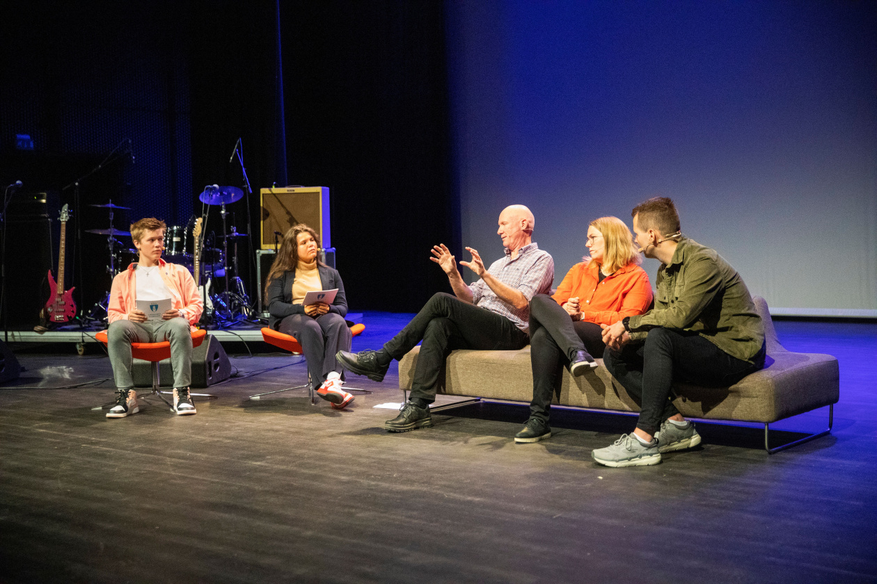 Young and older people on a stage exchanging ideias