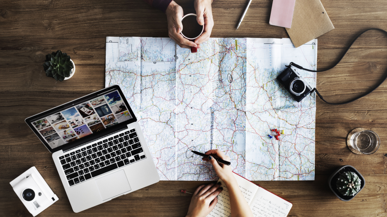 Two individuals are engaged in an activity on a wooden surface, featuring a map, a laptop, and various items.