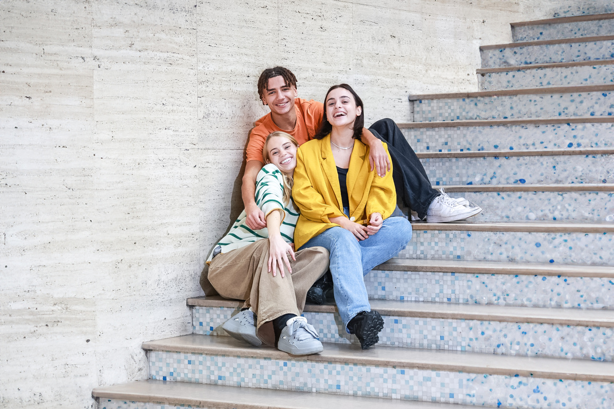 Three young people sitting in the stairs and hugging each other