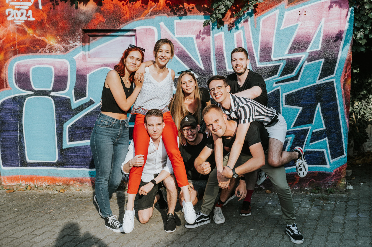 A group of young people outside, in front of a graffiti wall